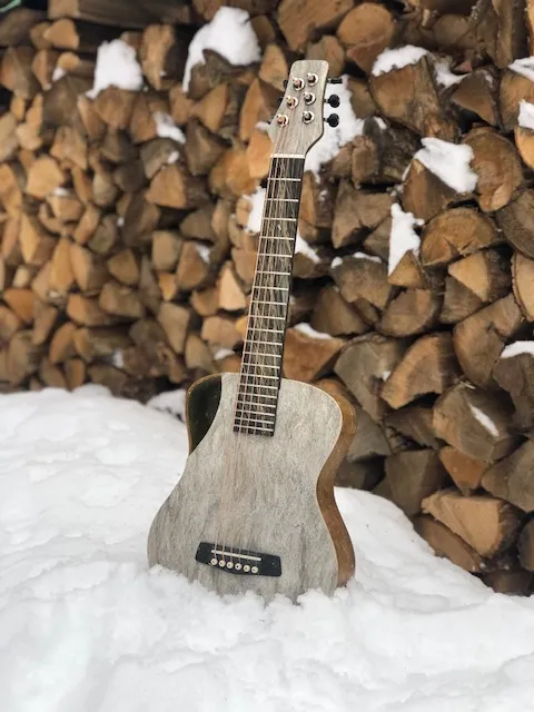 A guitar with a body made from hemp, standing in snow
